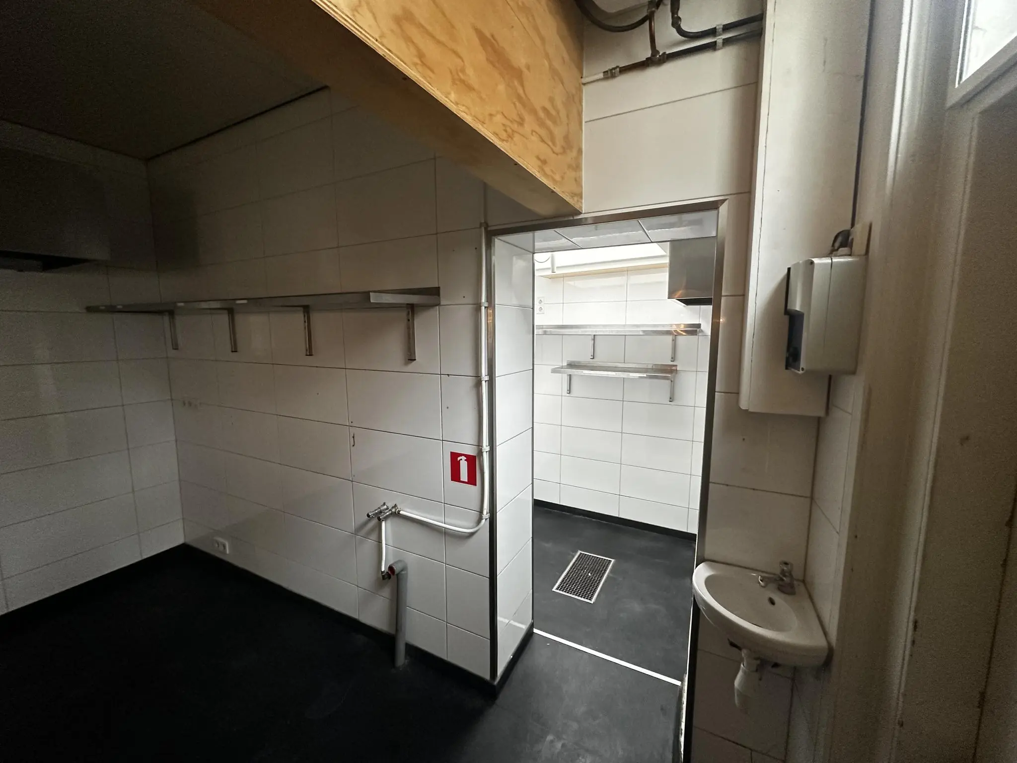 Lege, betegelde keukenruimte op het Sint Agathaplein met metalen wandrekken, gootsteentje en zicht op een tweede ruimte met ventilatieput.